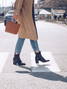 Stylish woman wearing straight leg jeans and ankle boots crossing the street.