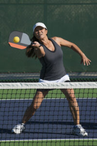 A woman mid-hit playing pickleball.