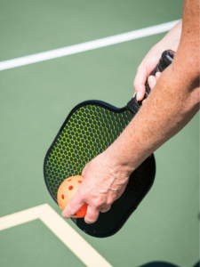 A close up shot of a pickleball paddle and ball preparing for a serve.
