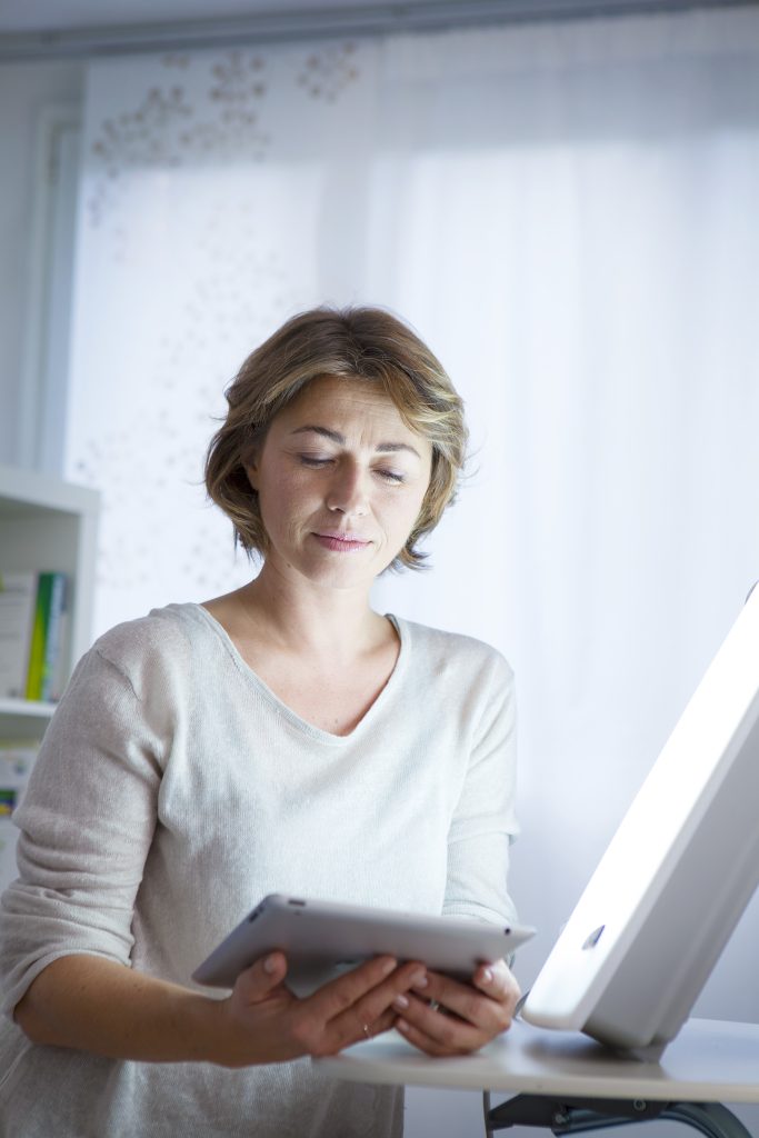 Woman combatting Seasonal Affective Disorder During Christmas with a light therapy lamp. 