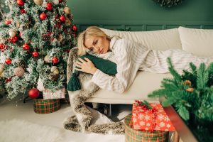 A woman looks serious while laying on couch in front of Christmas tree.