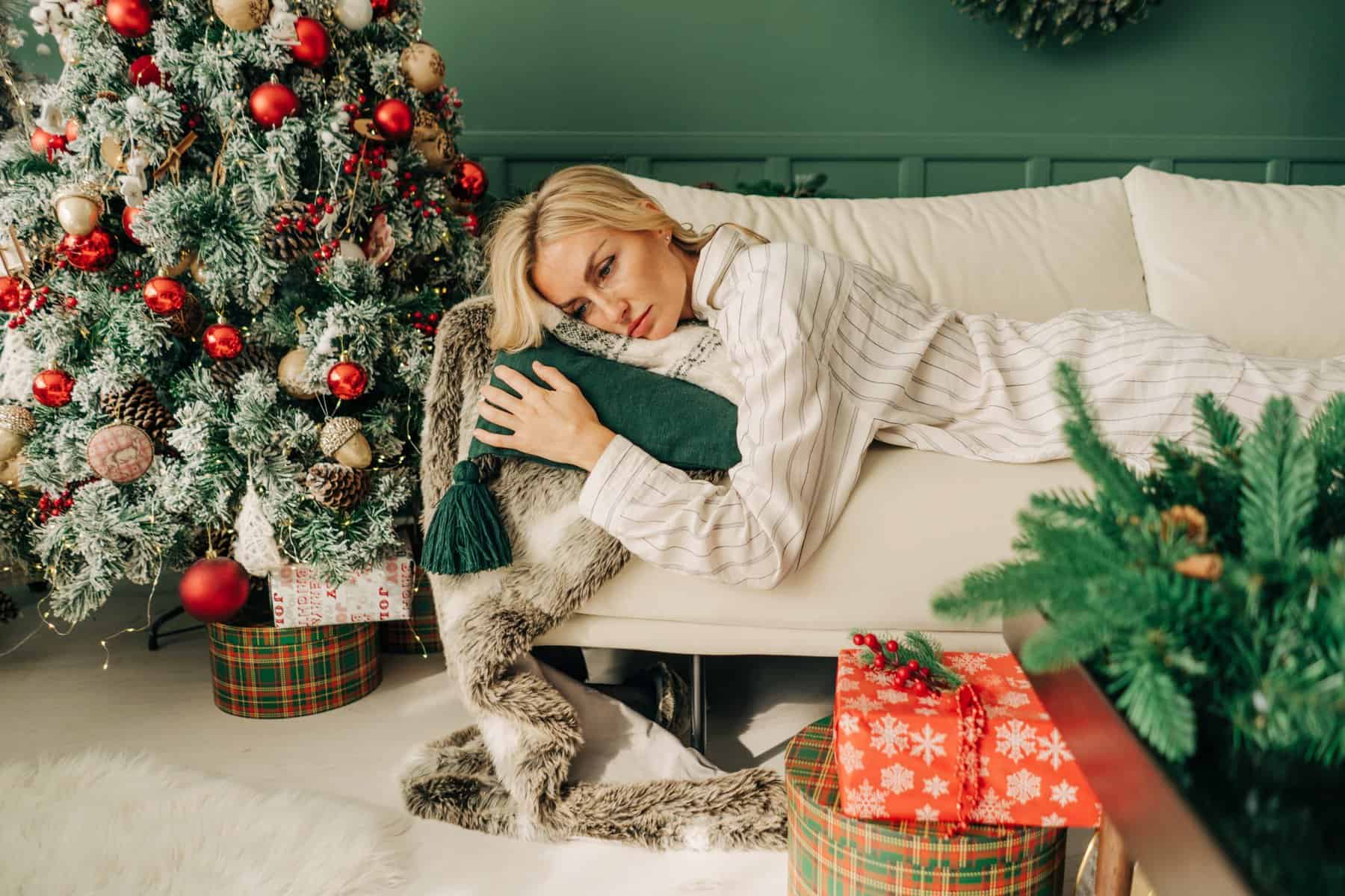 A woman looks serious while laying on couch in front of Christmas tree.