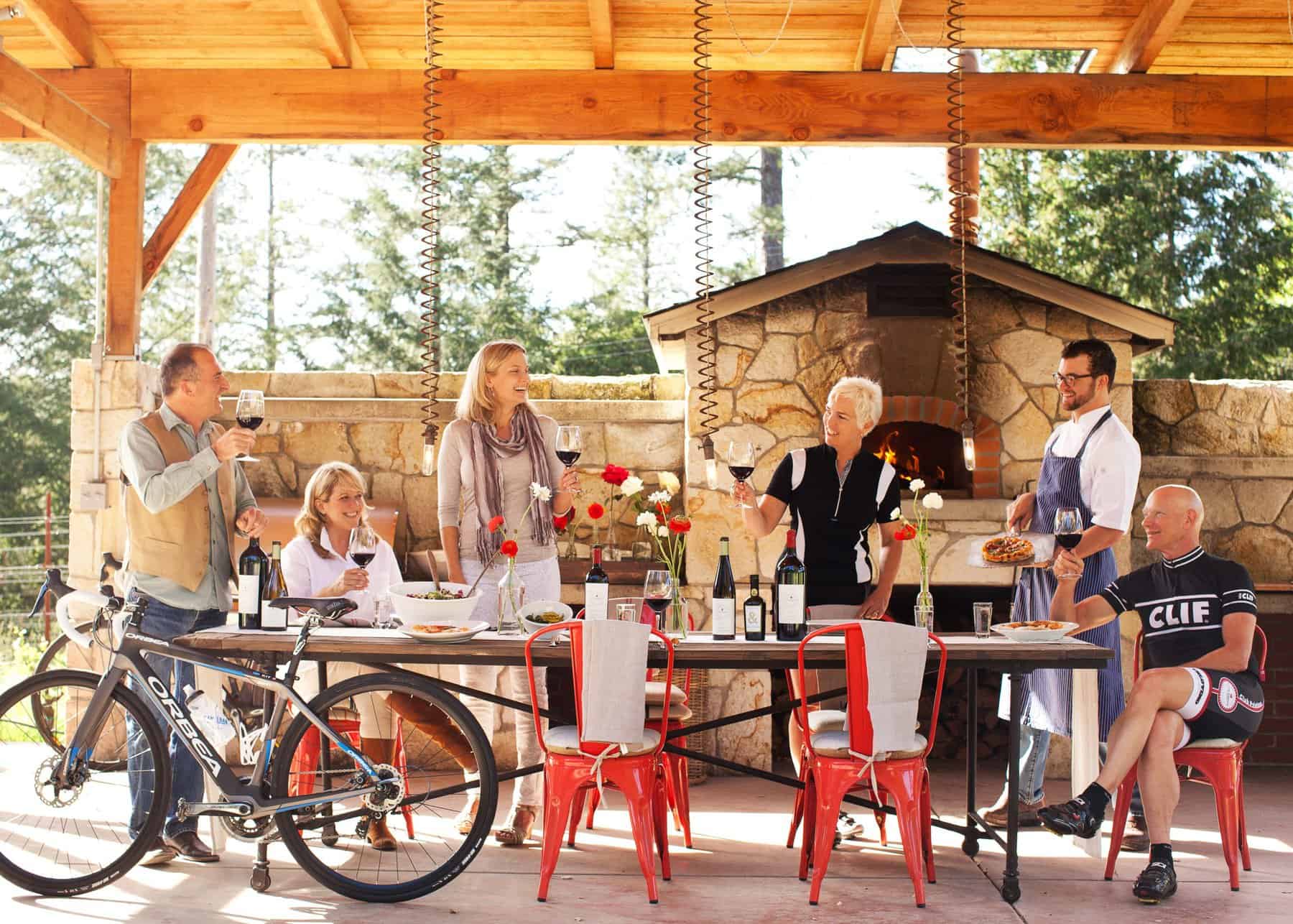 A group of people share a bottle of wine at a long, outdoor table at CLIF winery in Napa Valley.