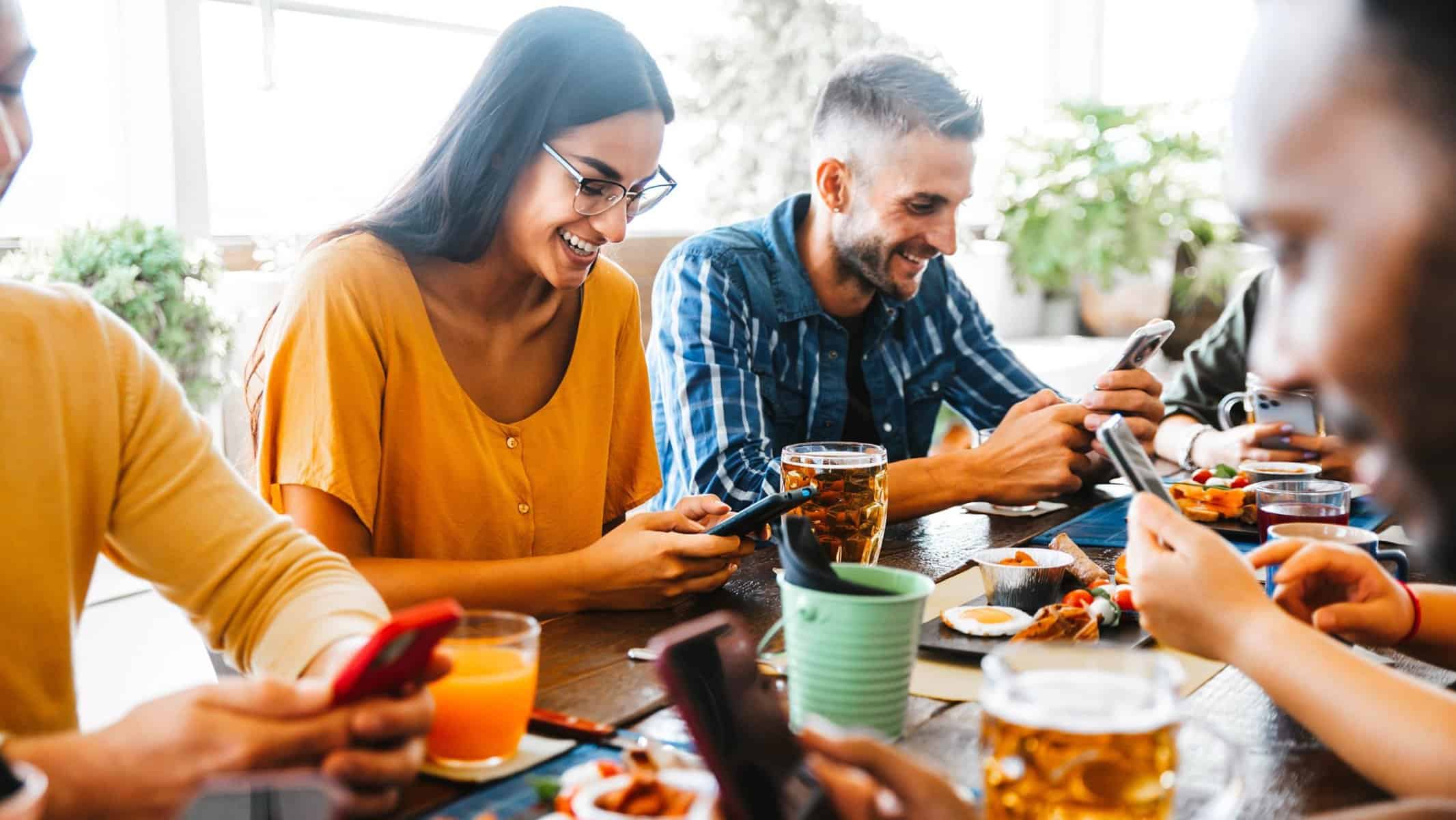 A large group of friends uses their cellphones at a table to Venmo the one person who paid the bill. 