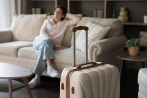 A recently shipped suitcase is in the foreground while a woman relaxes on the couch in the background. She is out of focus.