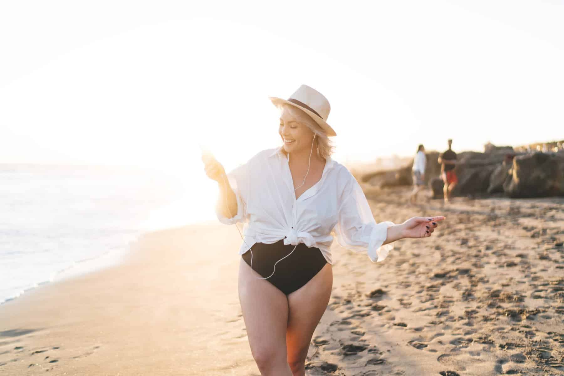 Curvy woman on the beach wearing a full-coverage swimsuit and a white coverup.
