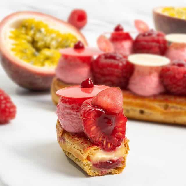 A cut eclair showing a custard and raspberry filling topped with raspberries. 
