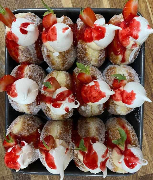 A tray of sugared doughnuts are stuffed with white cream and topped with strawberry sauce from Bread Ahead Bakery.