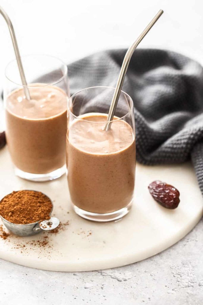 A thick chocolatey smoothie is styled beside cocoa powder and dates. 