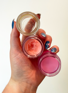 A hand is holding three containers of the Laniege Lip Mask on sale for Prime Day. Each is a different degree of used from an empty container to a fresh pot. 
