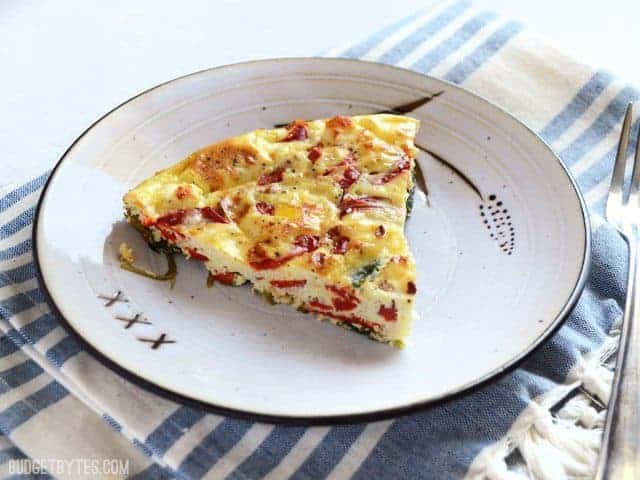 A slice of egg frittata with red peppers and spinach. 
