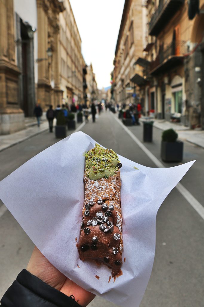 A hand holds up a cannoli in the streets of Palermo, Sicily. 