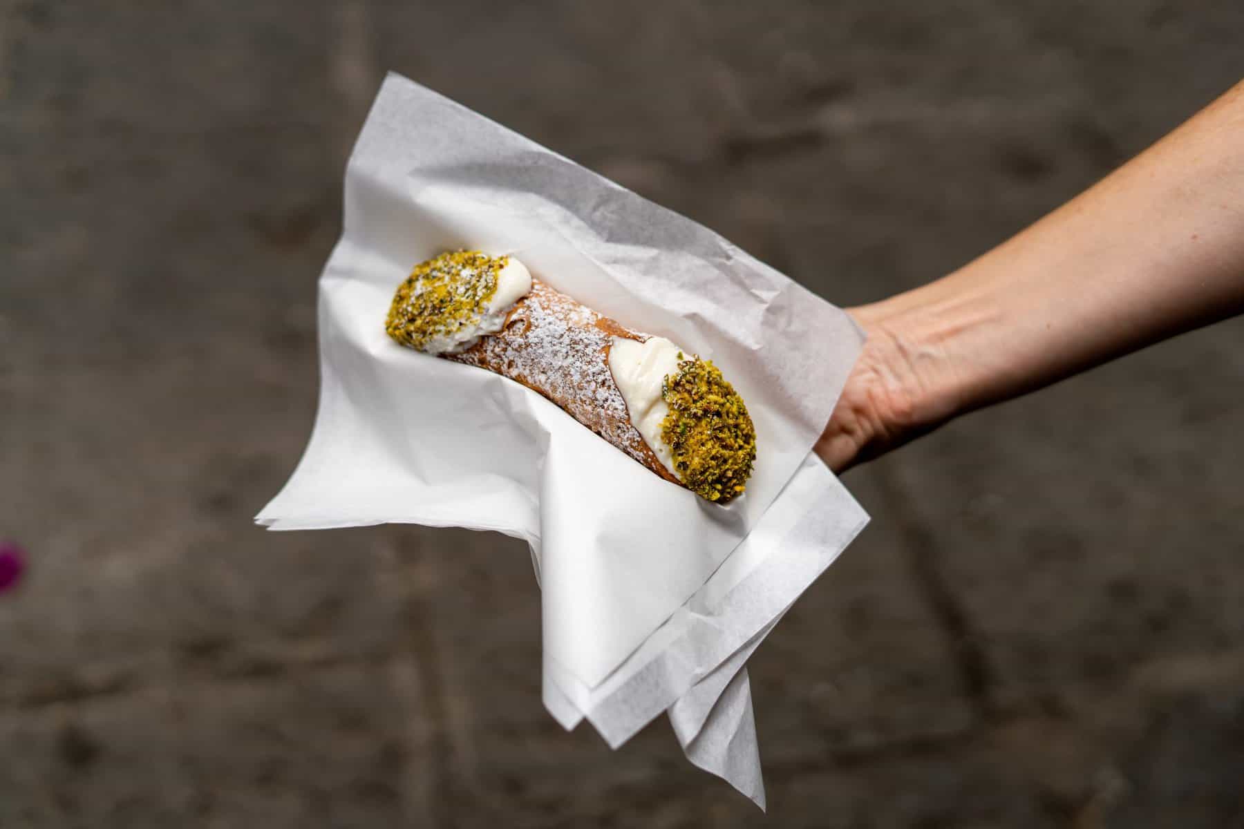 A hand is holding one of the best cannoli in Palermo.