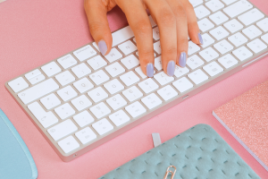 A woman's hands rest on her keyboard. She's surrounded by cute stationery.